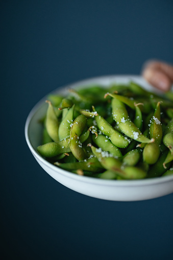 An anonymous Asian female chef serving edamame beans snack at home.