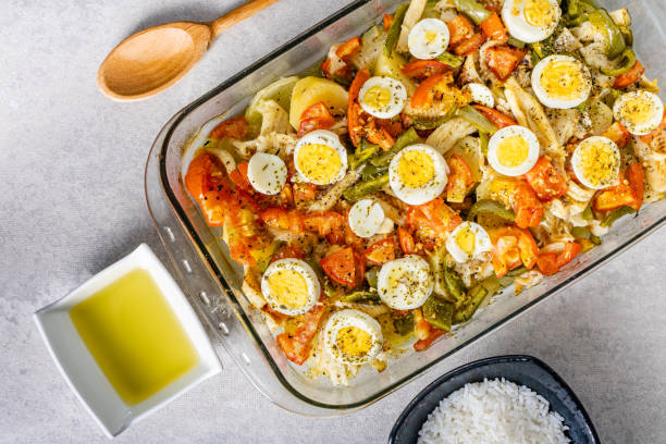 istock Gomes de sa codfish roasted in olive oil with tomatoes, peppers, onions, boiled eggs and oregano. In a rectangular glass baking dish. Detail wooden spoon and olive oil. 1475129649