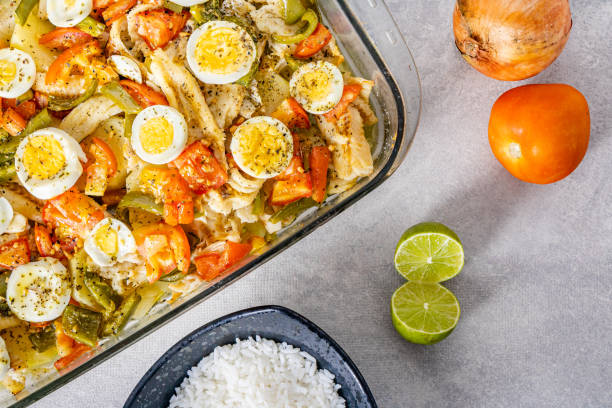 istock Gomes de sa codfish roasted in olive oil with tomatoes, peppers, onions, boiled eggs and oregano. In a rectangular glass baking dish. Detail wooden spoon and olive oil. 1475129814