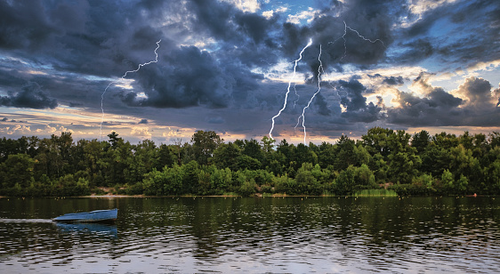 landscape empty boat on a forest lake-river under thunderclouds with lightning.