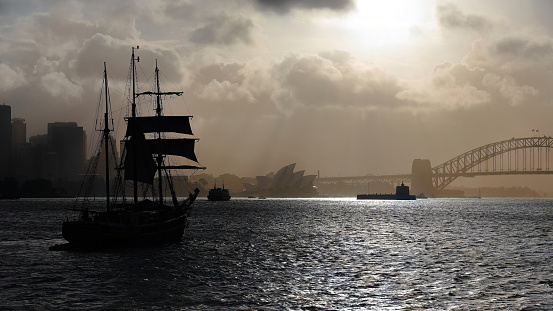 Silhouetted schooner tall ship sailing towards Harbour Bridge in a hazy afternoon. Sydney-Australia-562