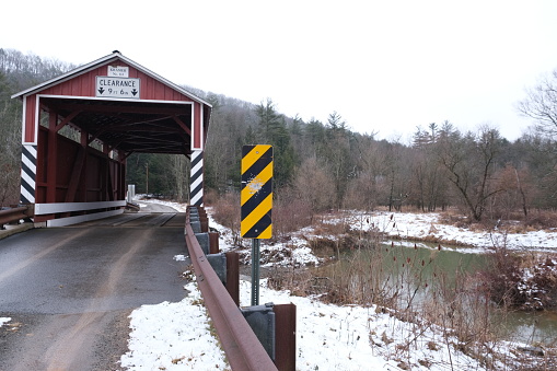 Historic red wooden Kramer covered bridge located in Columbia County Pennsylvania built over Mud Run creek.  It is 50' long built in 1881 with Queen Post truss construction.  Listed on the National Register of Historic Places.  Photographed just after a light snow against cloud skies.