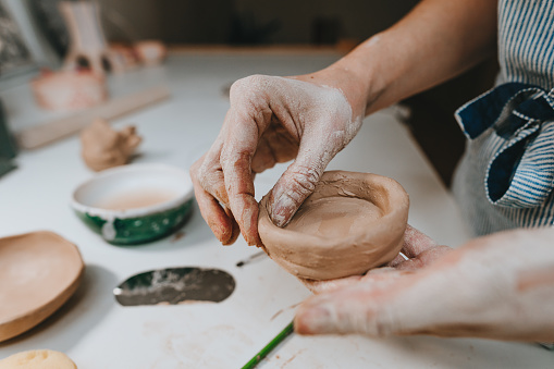 Cropped shot of a woman shaping a clay pot in her workshop