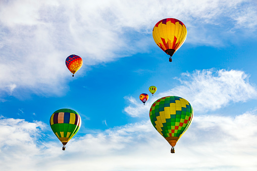This is a photograph taken at sunrise of five hot air balloons in Temecula California. The balloons have  a variety of beautiful bright colors.