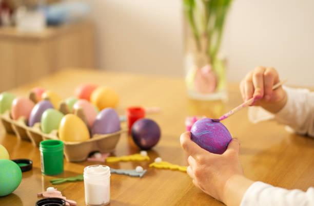 istock Child hands painting Easter eggs on wooden table. 1475133707