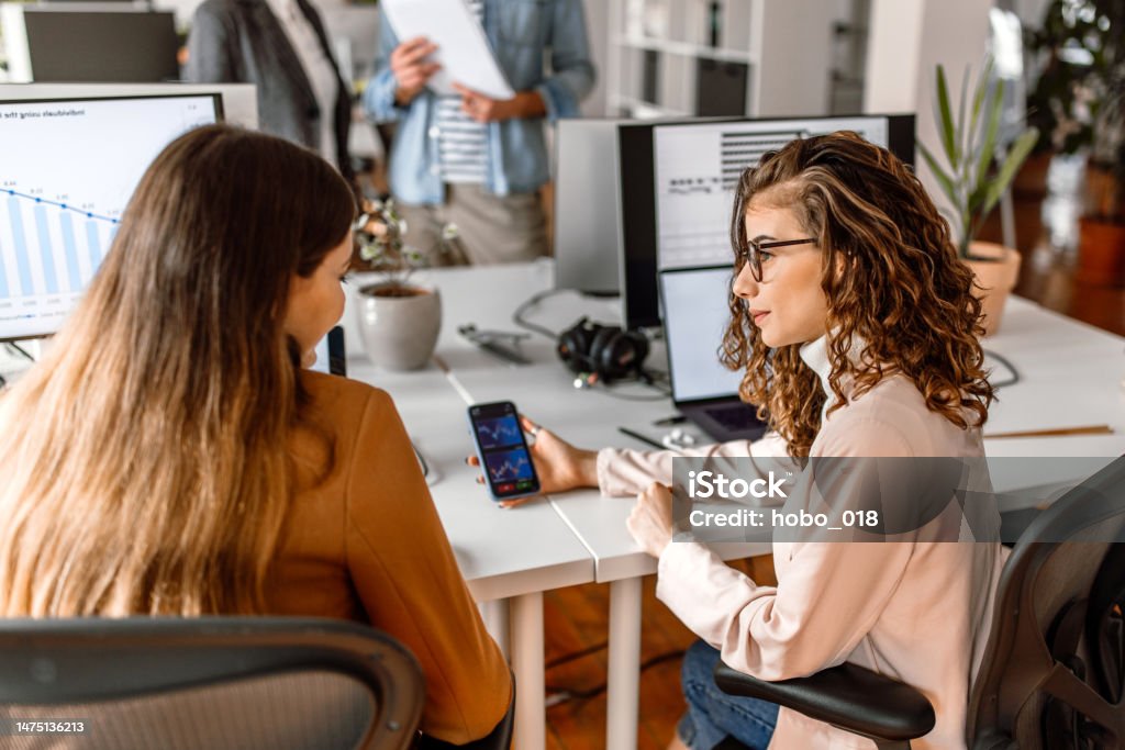Colleagues analysing crypto stock market in the office Two women in the office analysing crypto stock market, using mobile app 20-24 Years Stock Photo