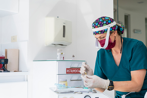 Beautiful Latino dentist from Bogota Colombia between the ages of 40 and 49 arriving at the office and preparing the dental fixtures while wearing her uniform