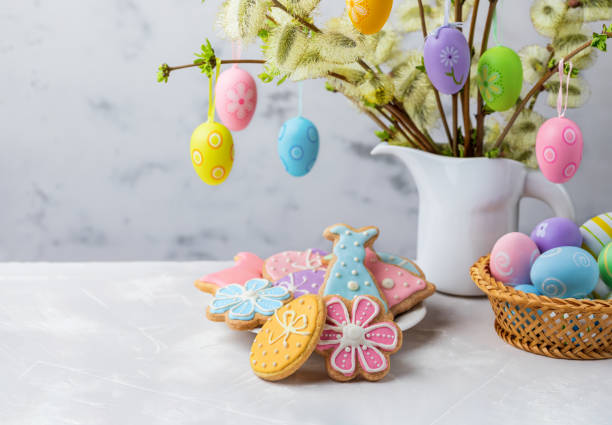 Easter composition with homemade Easter gingerbread cookies and colorful Easter eggs. Homemade Easter gingerbread cookies shaped of Easter bunny, egg and flower, colorful eggs in a basket and flowering willow decorated with Easter eggs on a table for festive Easter celebration at home. Copy space. easter cake stock pictures, royalty-free photos & images