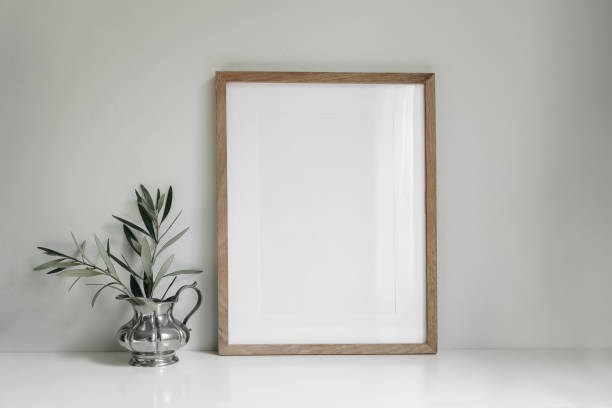 istock Blank vertical wooden picture frame mockup. Olive tree branches in silver jug vase. Sage green wall background. Working space, home office. Art, poster display. Retro summer interior still life. 1475145958
