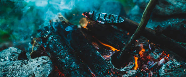 istock Vivid smoldered firewoods burned in fire close-up. Atmospheric warm background with orange flame of campfire and blue smoke. Wonderful full frame image of bonfire. Burning logs in beautiful fire. 1475150318