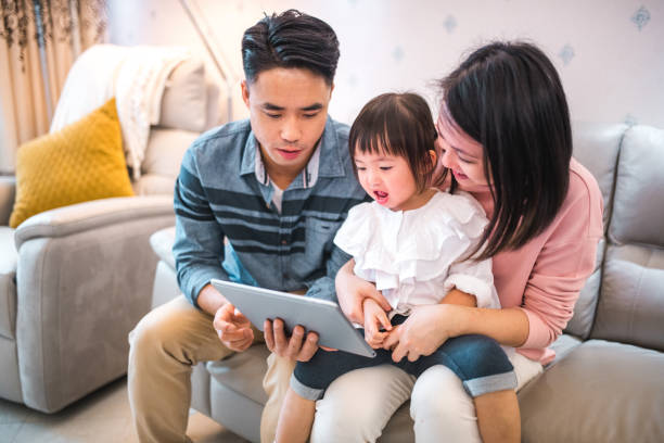 istock Affectionate Young Asian Parents With One Daughter Using A Digital Tablet At Home 1475152243