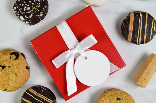 Closeup of red present with blank white tag surrounded by tempting cookies.
