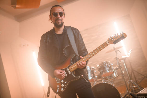 Hispanic guitarist playing guitar and recording music in recording studio. Waist-up shot, looking at camera.
