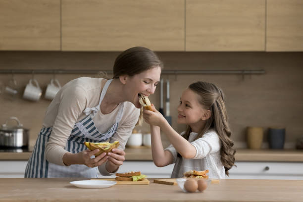 Joyful little kid girl giving mom sandwich to bite stock photo