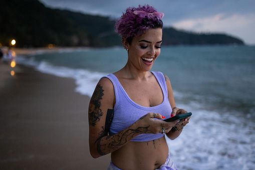 One woman, beautiful Latin woman using smart phone on the beach by the sea in dusk.