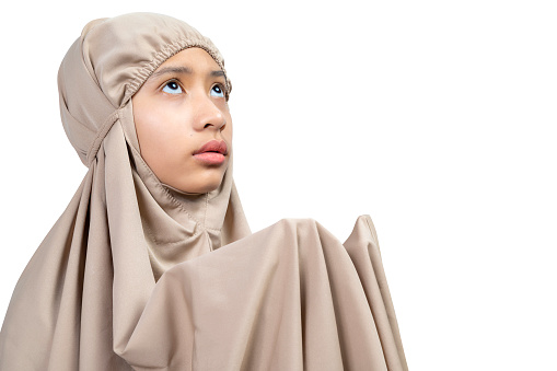 Asian Muslim girl in a hijab raising hands and praying isolated over white background