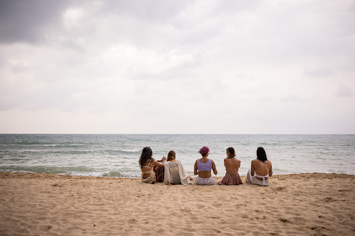 Group of people, women and transgender persons on the beach by the sea together.