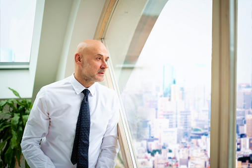Shot of worried businessman wearing shirt and tie and looking thougthful while standing at the window.