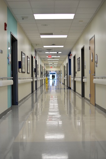 The long silent hallway of a hospital with some workers at the end