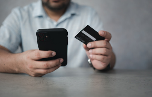 Man hand holding black credit card and using a smartphone for mobile payment, online shopping concept. People relax on holiday use technology from smartphones for the convenience of daily use
