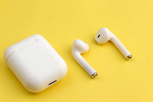 Modern white wireless bluetooth earphones with charging case isolated on yellow background.