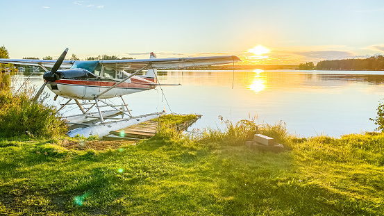 As the sun sets in Anchorage,Alaska, the colors play across the waters of Lake Hood. This lake is used as a runway for float planes.  It offers a stunning view.  As the airplane sits parked alongside the lake, the stunning sunset make for a great backdrop.