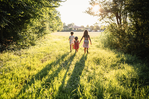 rear view of three children running towards sun in the field