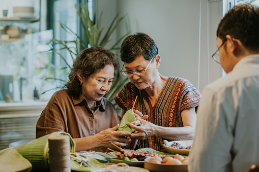 Thais senior woman teaching her sister to wrapping a nature package , eco friendly that make from banana leaf, wrapping grilled pork with sticky rice, preparing for open delivery restaurant.