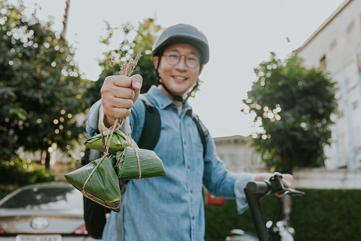 Service mind with Asian delivery man in helmet with electric scooter showing natural package that made from banana leaf that use for wrapping a food.