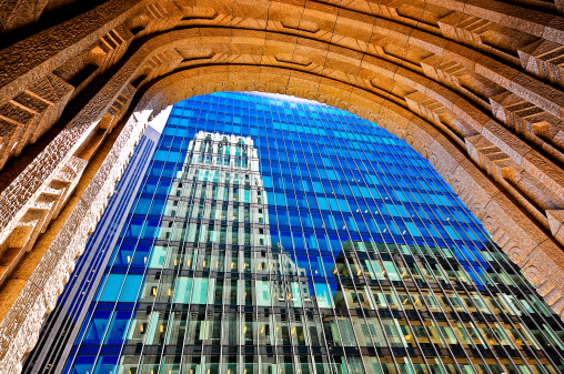 Historic building reflected in the windows of a modern building framed in an archway.