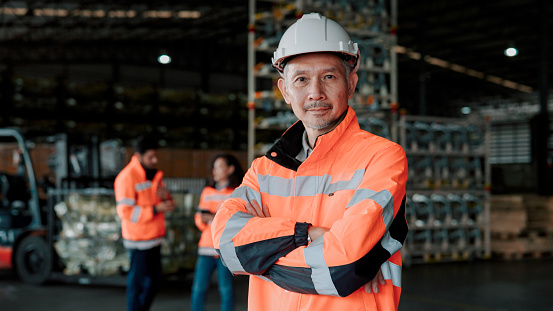 An adult warehouse manager looking at the camera after supervising another two workers on how to manage merchandise in the workplace.