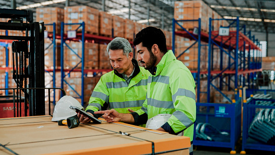 A male Asian warehouse manager talking to a younger worker about how to improve their work process.