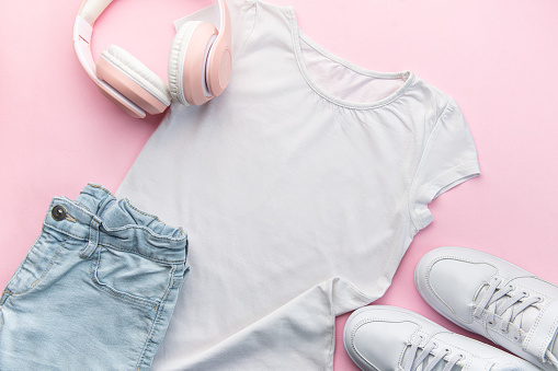 Child's white t-shirt, white sneakers and headphones on pink backgrund.