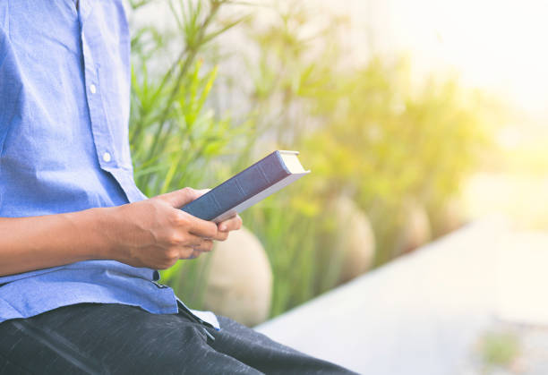 istock Closeup man holding book or bible with sunlight and nature background. 1475198512