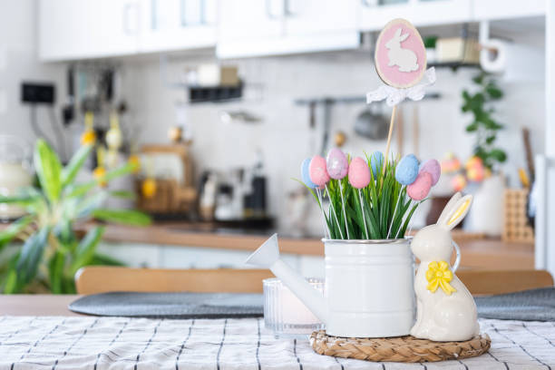 istock Easter decoration of colorful eggs in a basket and a rabbit on the kitchen table in a rustic style. Festive interior of a country house 1475198654