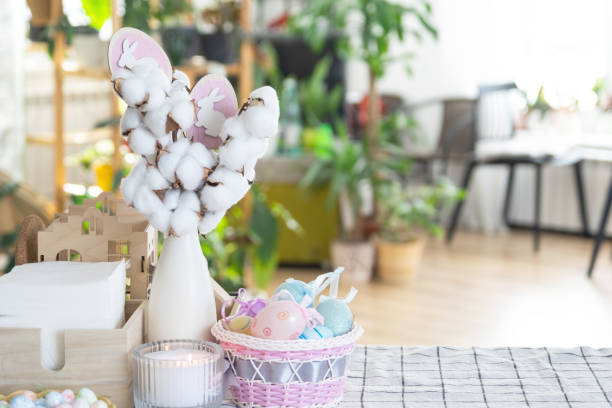 istock Easter decoration of colorful eggs in a basket and a rabbit on the kitchen table in a rustic style. Festive interior of a country house 1475198714