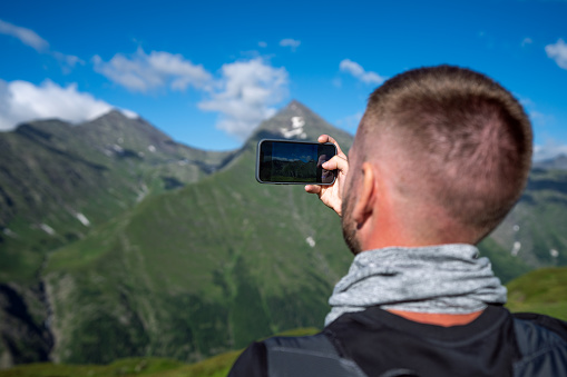 Rear view of a man taking picture with a smartphone in the mountains