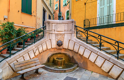 Small square with an old fountain and a bench in the Old Town of Villefranche sur Mer on the French Riviera, South of France