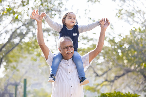 Carefree granddaughter carrying granddaughter on shoulders at park