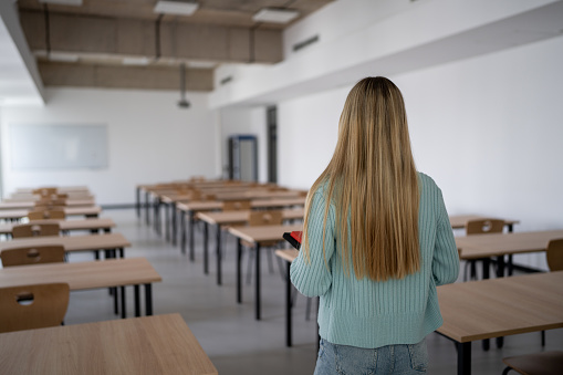 Female university student holding book while entering the empty classroom