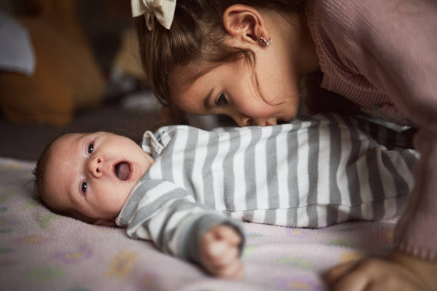 Lifestyle portrait of cute Caucasian girls sisters holding little baby on bed. Family love bonding together concept