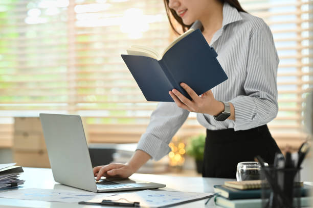 istock Cropped shot of female employee checking her working schedule plan and using laptop at workstation. 1475217079