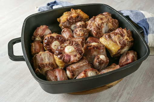 Roasted oxtail pieces with bone in a black tray fresh from the oven, gelatin-rich meat for a slow-cooking stew or traditional oxtail soup, copy space, selected focus, narrow depth of field