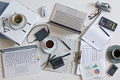 Top view of a full business desk with laptops, accounting papers, calculator, coffee and other office supplies, success work or stress concept, high angle shot from above