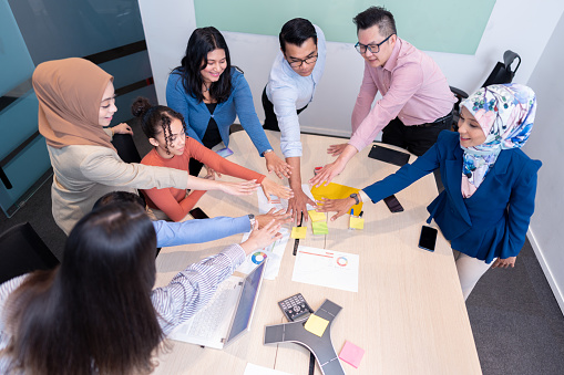 Co-workers stacking their hands together as symbol of unity on conference table