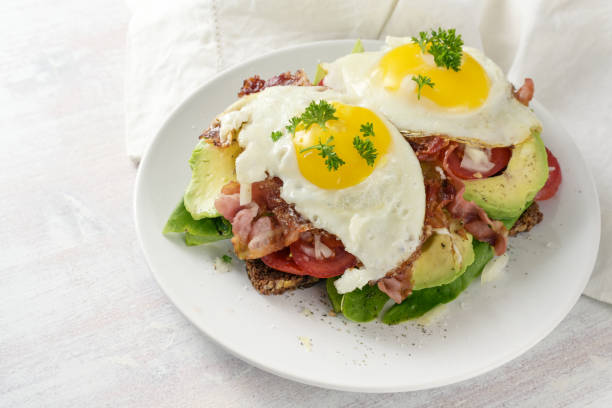 istock Fried egg, bacon and avocado on a dark whole meal bread with lettuce and tomato, delicious breakfast sandwich, light background, copy space, selected focus 1475218723