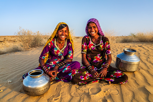 Indian girls crossing sand dunes and carrying on their heads water from local well, Thar Desert, Rajasthan, India. Rajasthani women and children often walk long distances through the desert to bring back jugs of water that they carry on their heads.