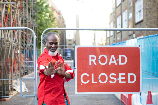 Mature man by a construction site in the London Docklands area. He is wearing a red shirt