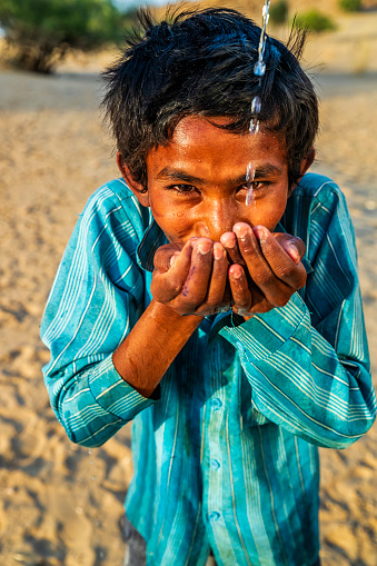 Indian young boy is drinking fresh water, desert village, Thar Desert, Rajasthan, India. Potable water is very precious on the desert - Rajasthani women and children often walk long distances through the desert to bring back jugs of water that they carry on their heads.