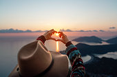 Travel in her heart. Woman makes heart from fingers looking at sea and islands at sunset